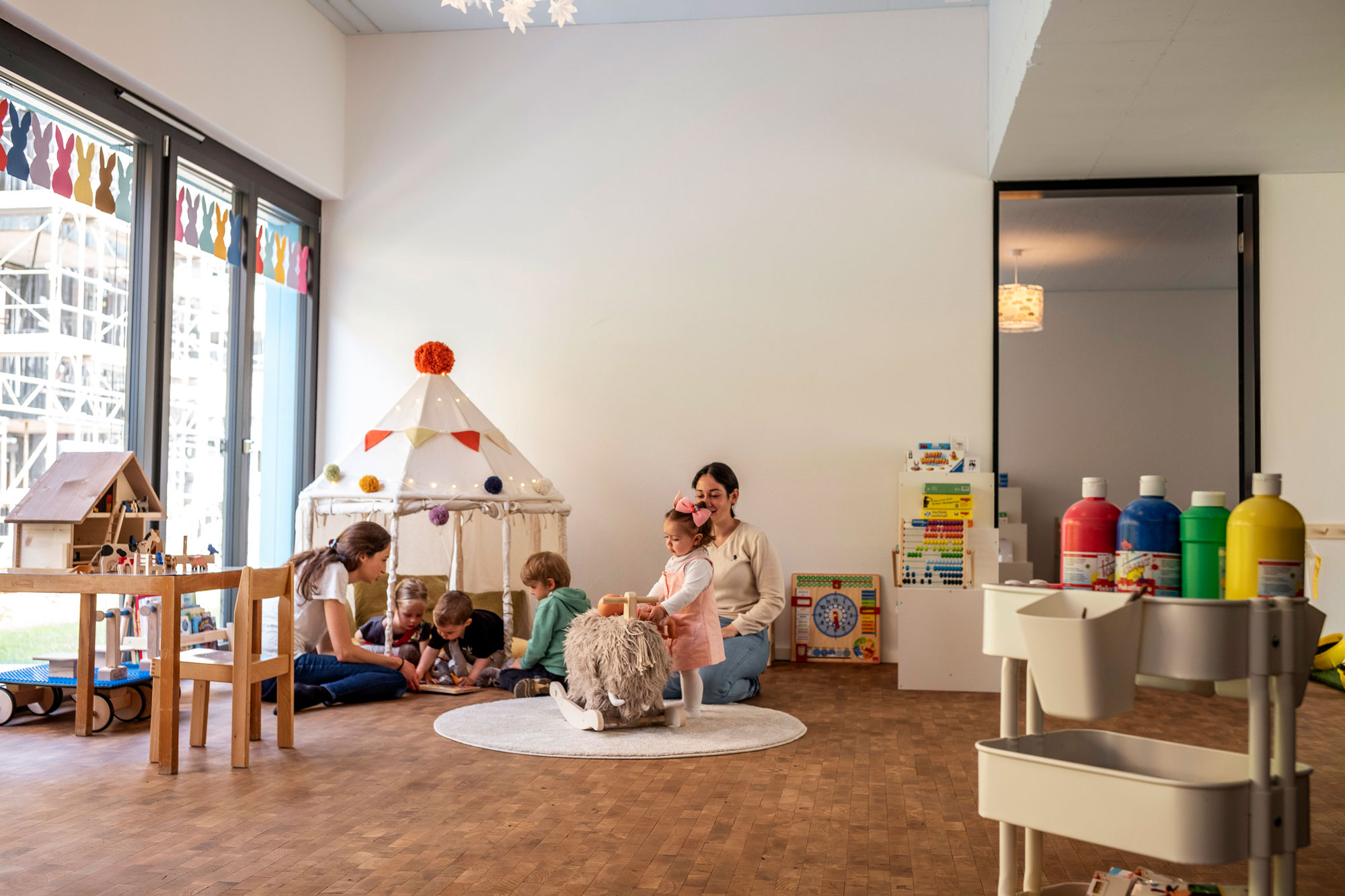 Zwei Betreuerinnen spielen mit vier Kindern auf dem Boden im Atelier Brüderhof.