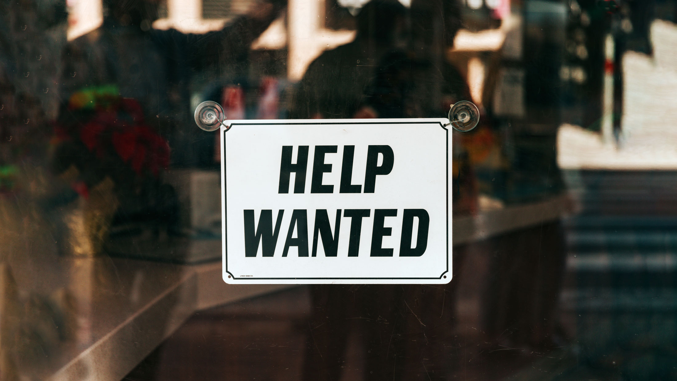 Symbolbild zum Employer Branding: Ein Schild mit der Aufschrift "Help wanted" steht in einem Schaufenster.